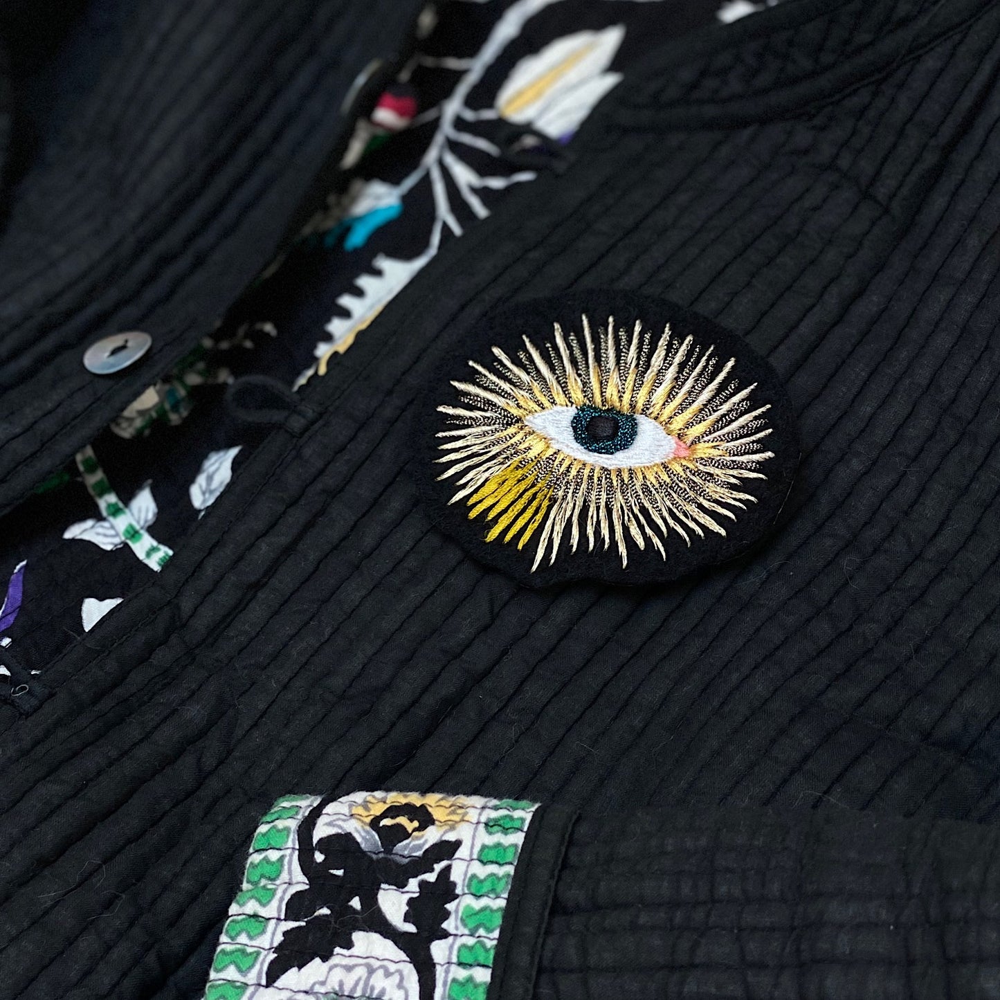 Close-up of metallic eye embroidered patch on black quilted jacket