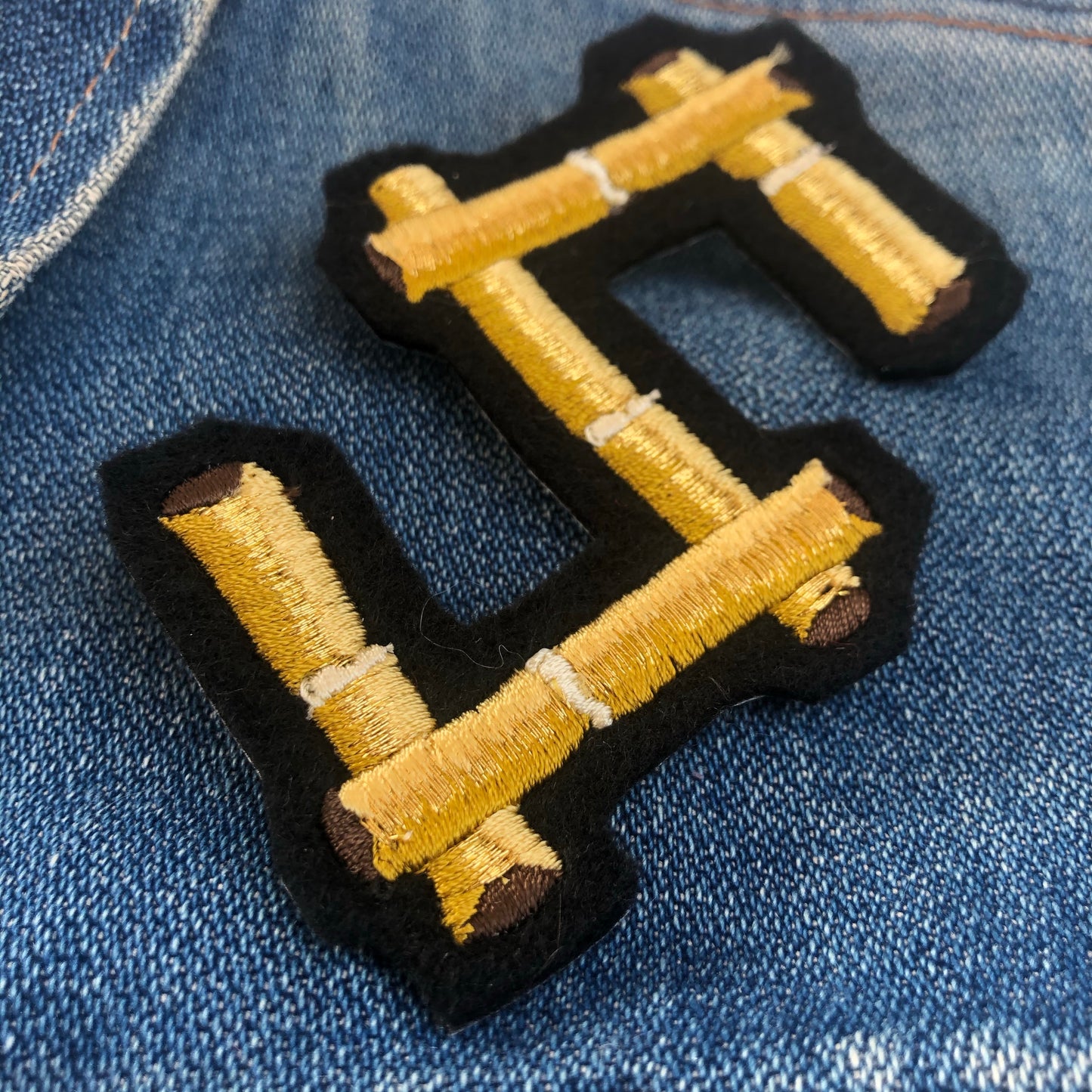 Close-up of bamboo embroidered letter S on the front shoulder of a blue denim jacket