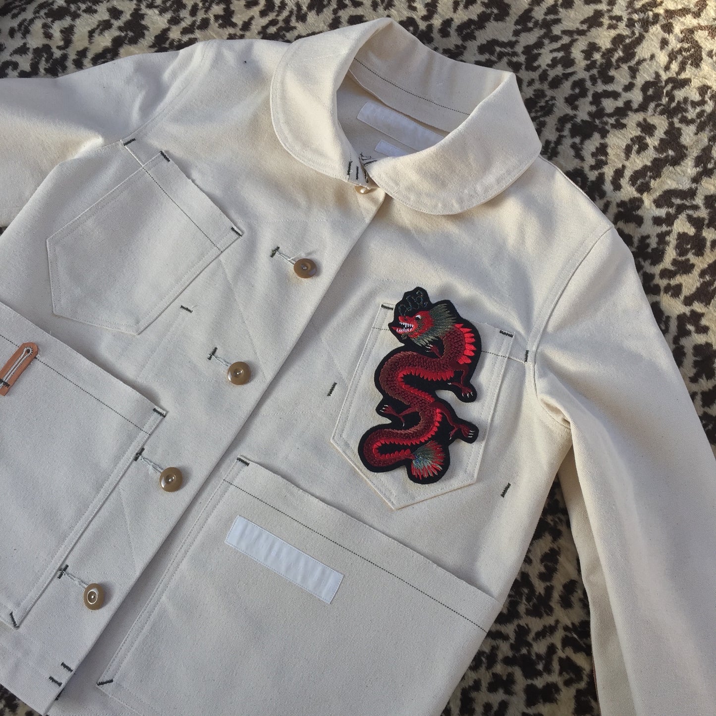 Dragon embroidered patch shown on front pocket of white denim jacket