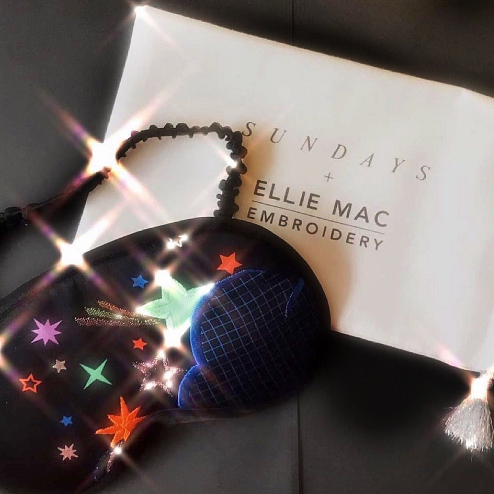 Disco nap eye mask and a white postcard which readys 'Sundays + Ellie Mac Enbroidery', both items are posed on a dark background
