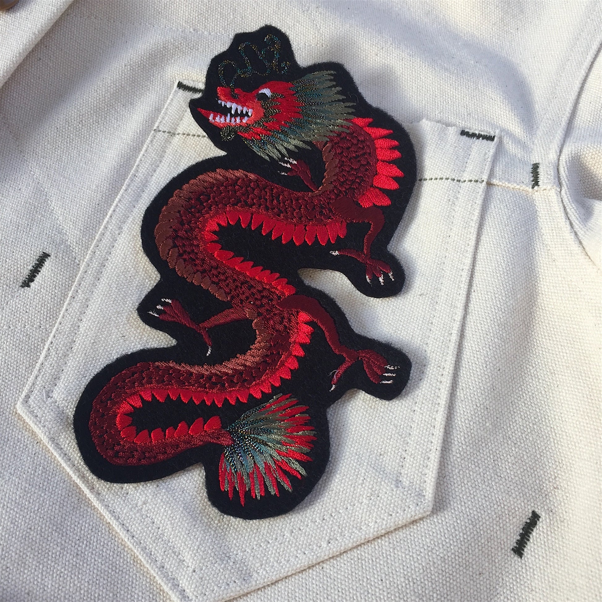Close-up of dragon embroidered patch shown on pocket of white denim jacket