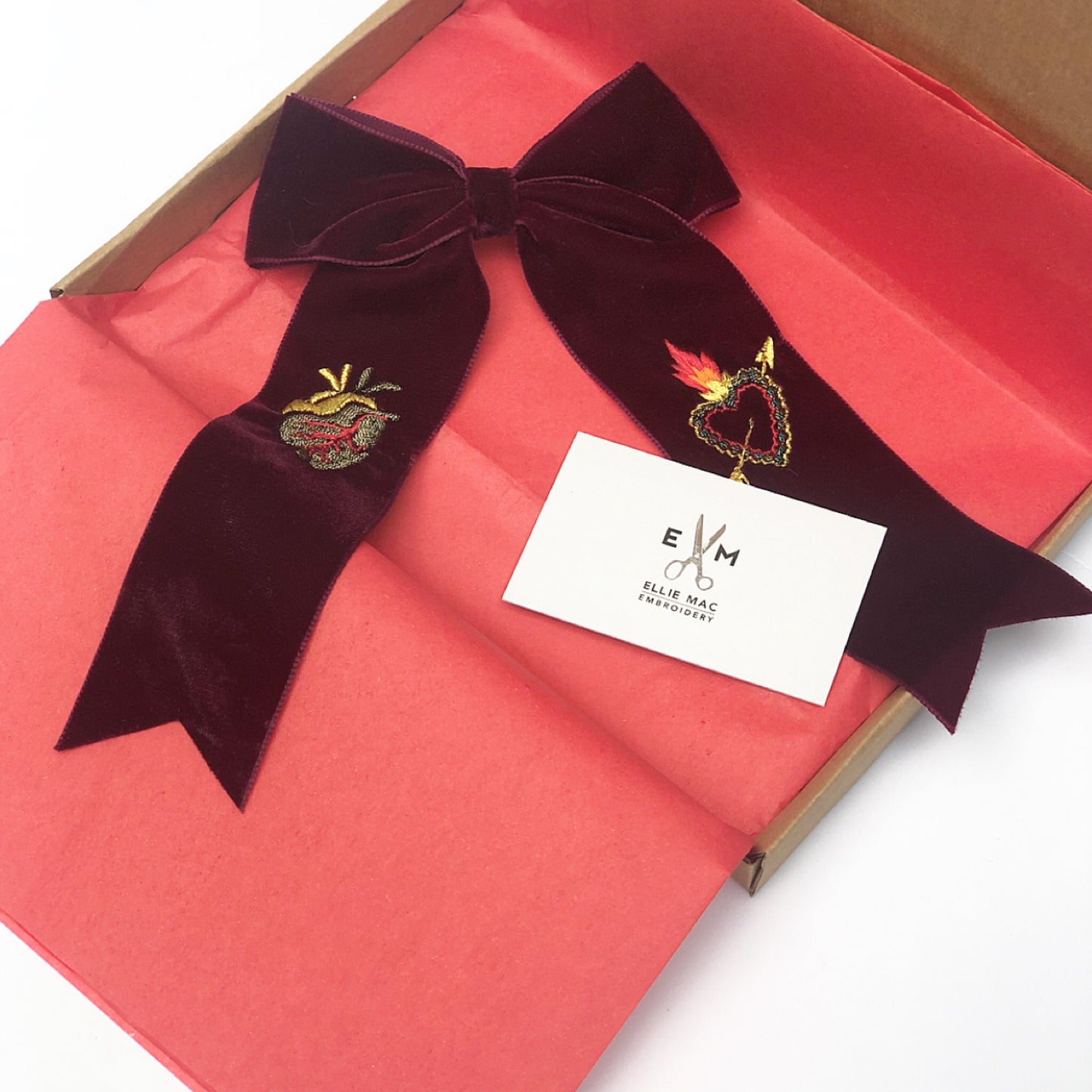 Maroon velvet hair bow in a small open brown box with salmon pink tissue paper