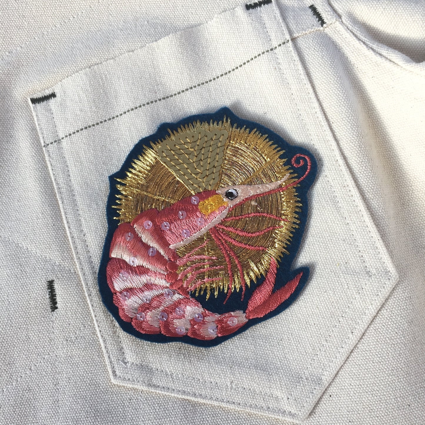Close-up of luxe embroidered king prawn patch on pocket of white deninm jacket
