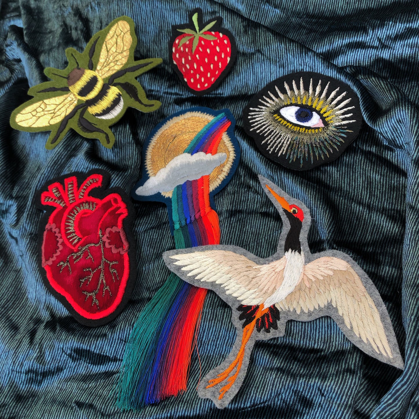 Selection of Ellie Mac embroidered patches on a blue metallic background. Included is strawberry, velvet heart and metallic eye