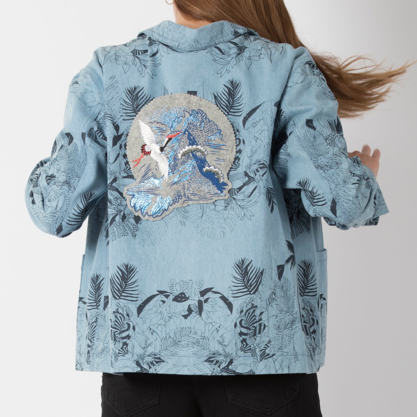 Foil printed & embroidered mountain crane patch shown on the back of a patterened light blue denim jacket