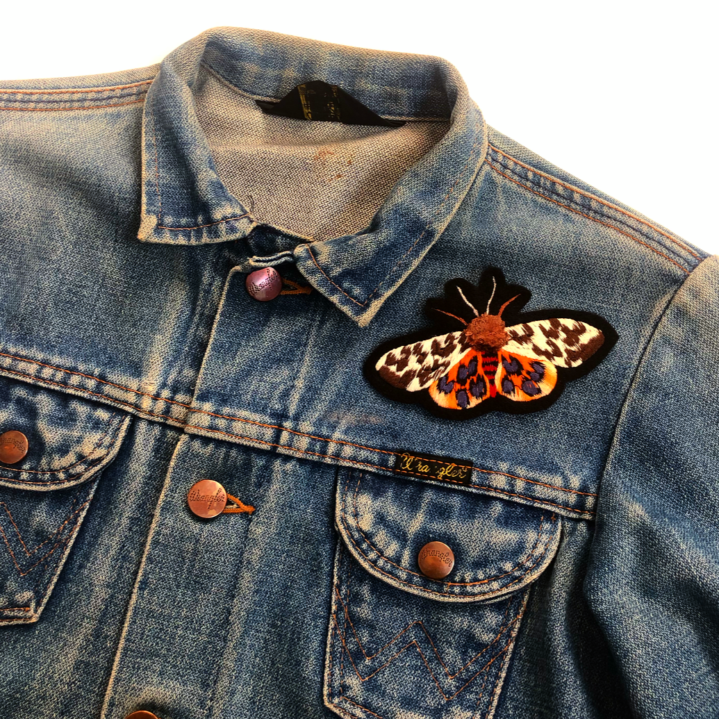 Pom-pom tiger moth embroidered patch on front shoulder of blue denim jacket