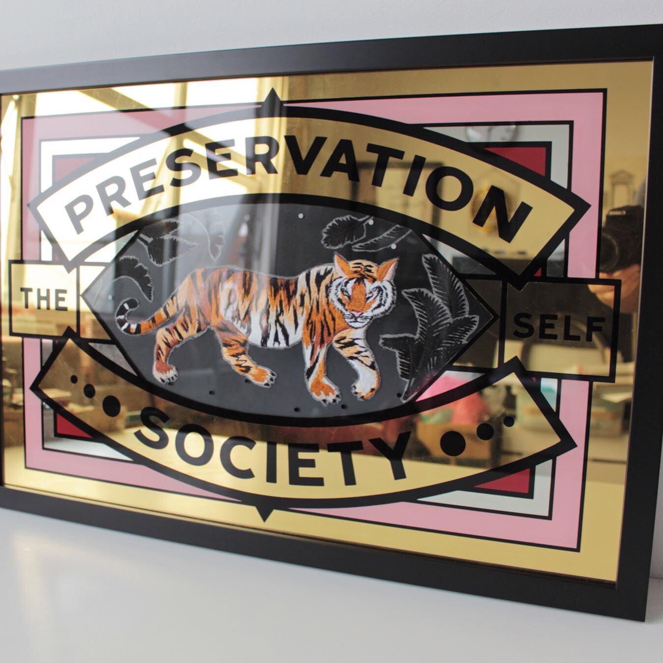 Embroidered prowling tiger and gold leaf artwork shown in black frame on white background