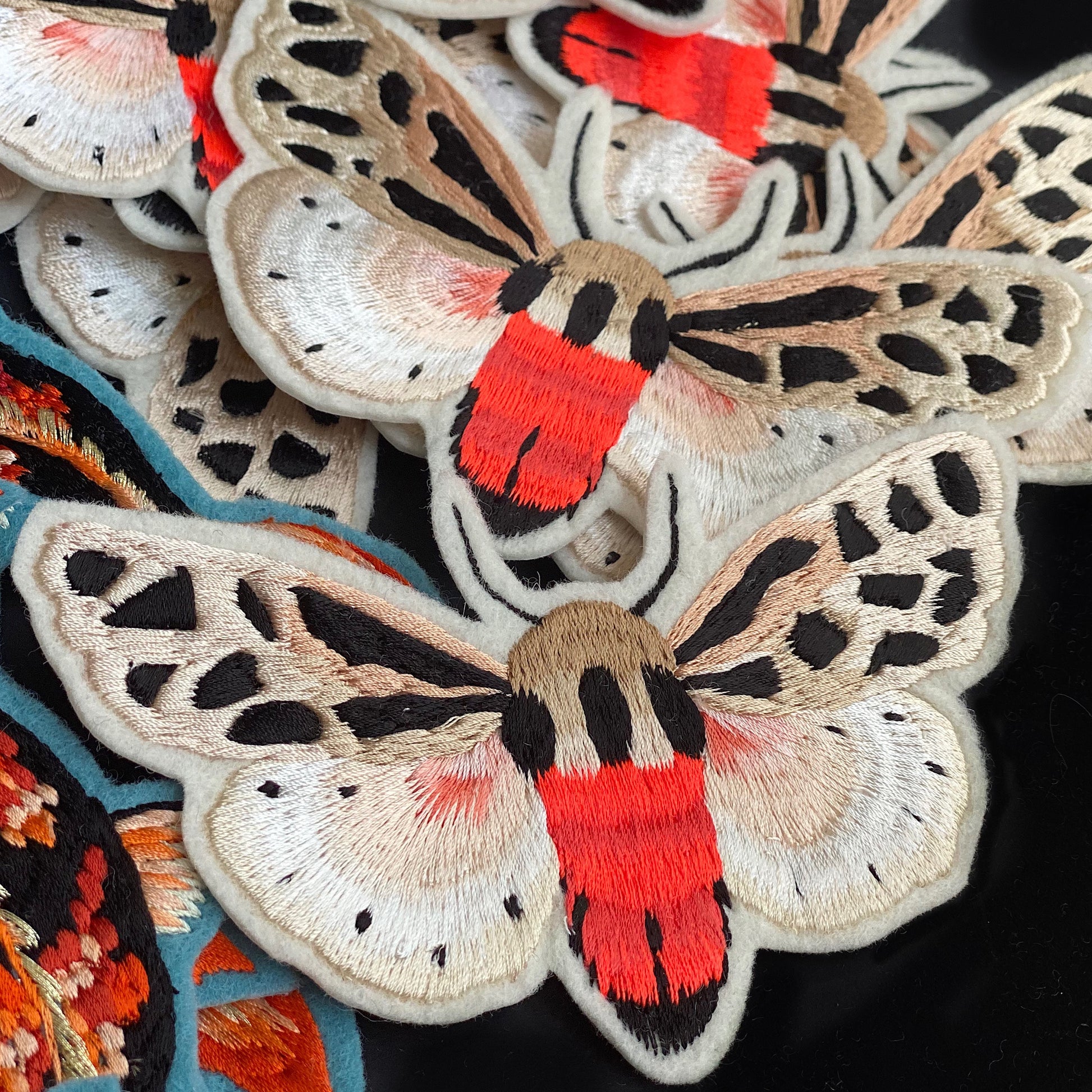 Collection of neon tiger moth embroidered patches layered on top of each other