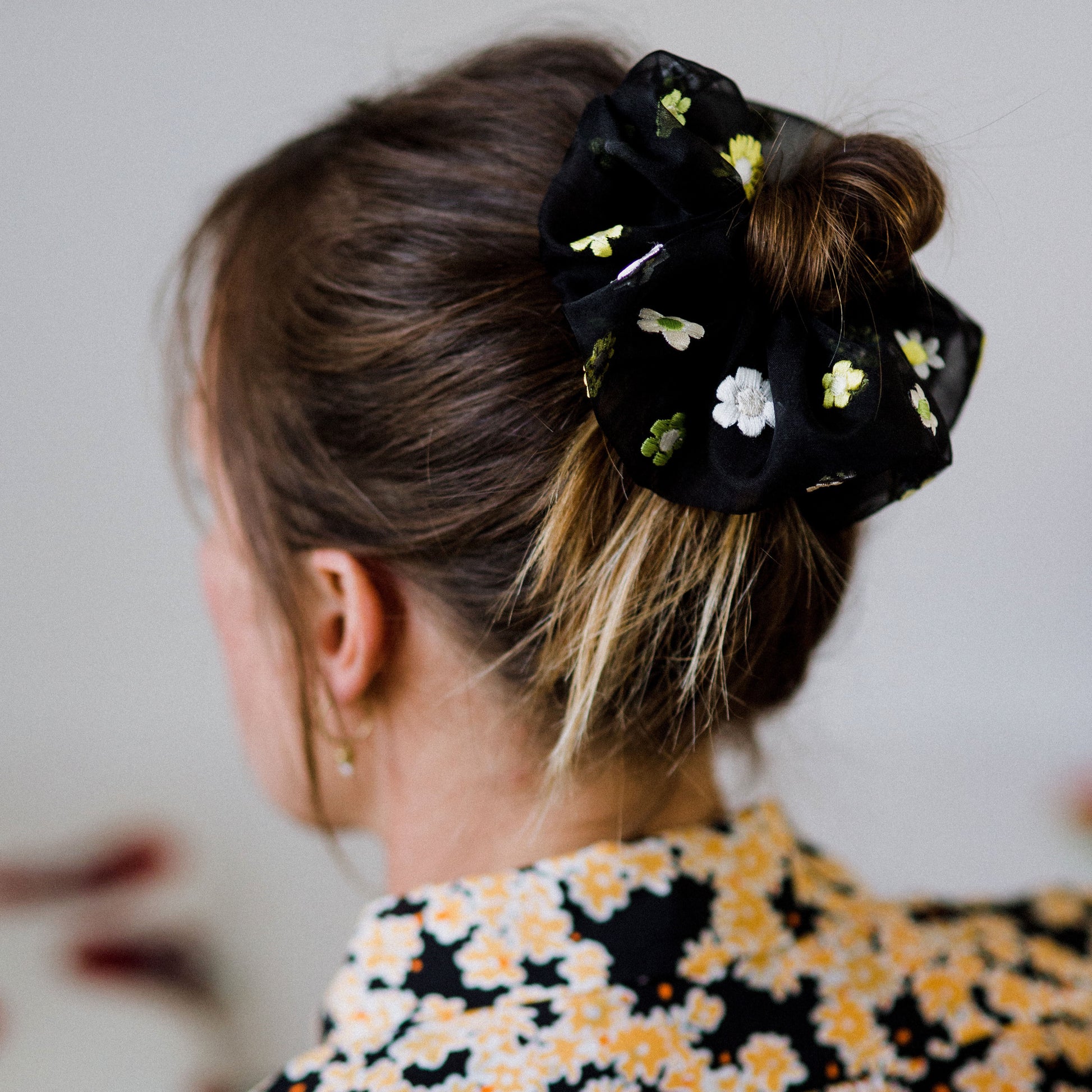 The back of a persons head, their head and shoulders visible, with the silk organza embroidered scunchie around their hair bun