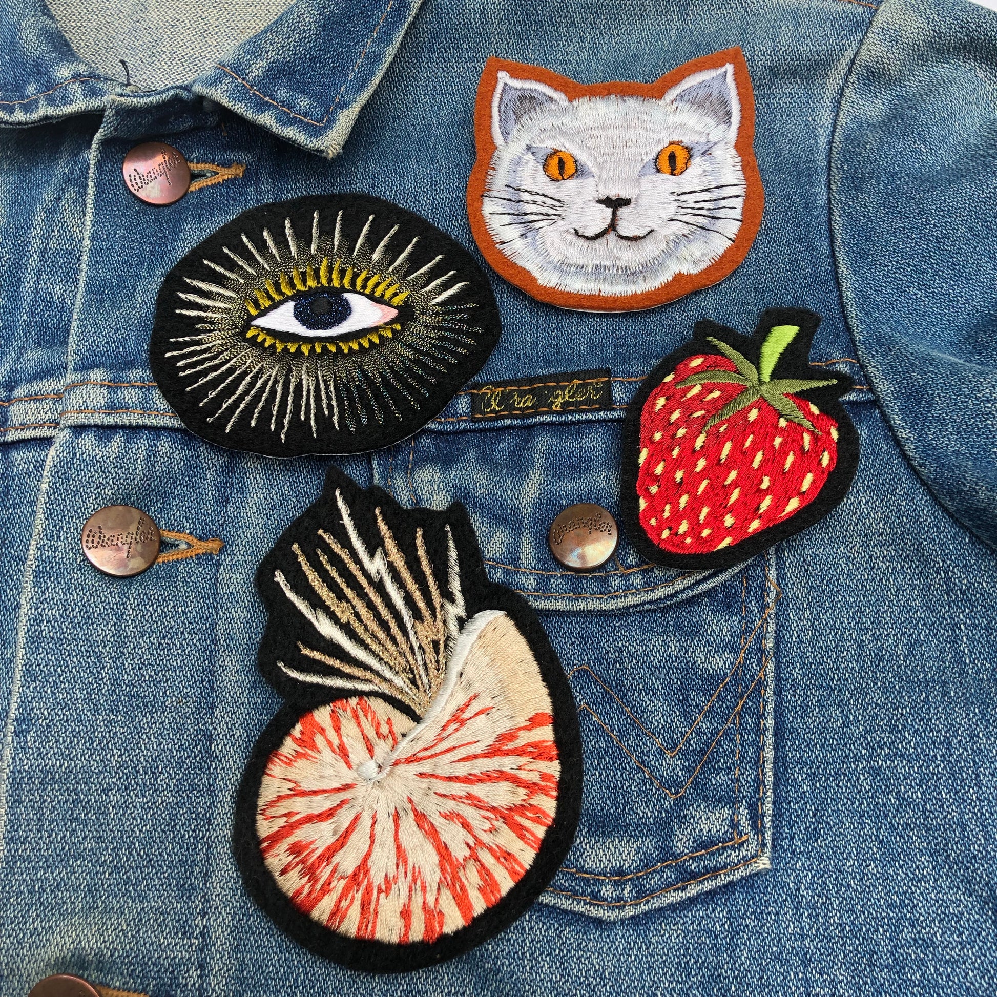 Selection of Ellie Mac Embroidery patches on a denim jacket including fat cat, metallic eye, strawberry and nautilus patches