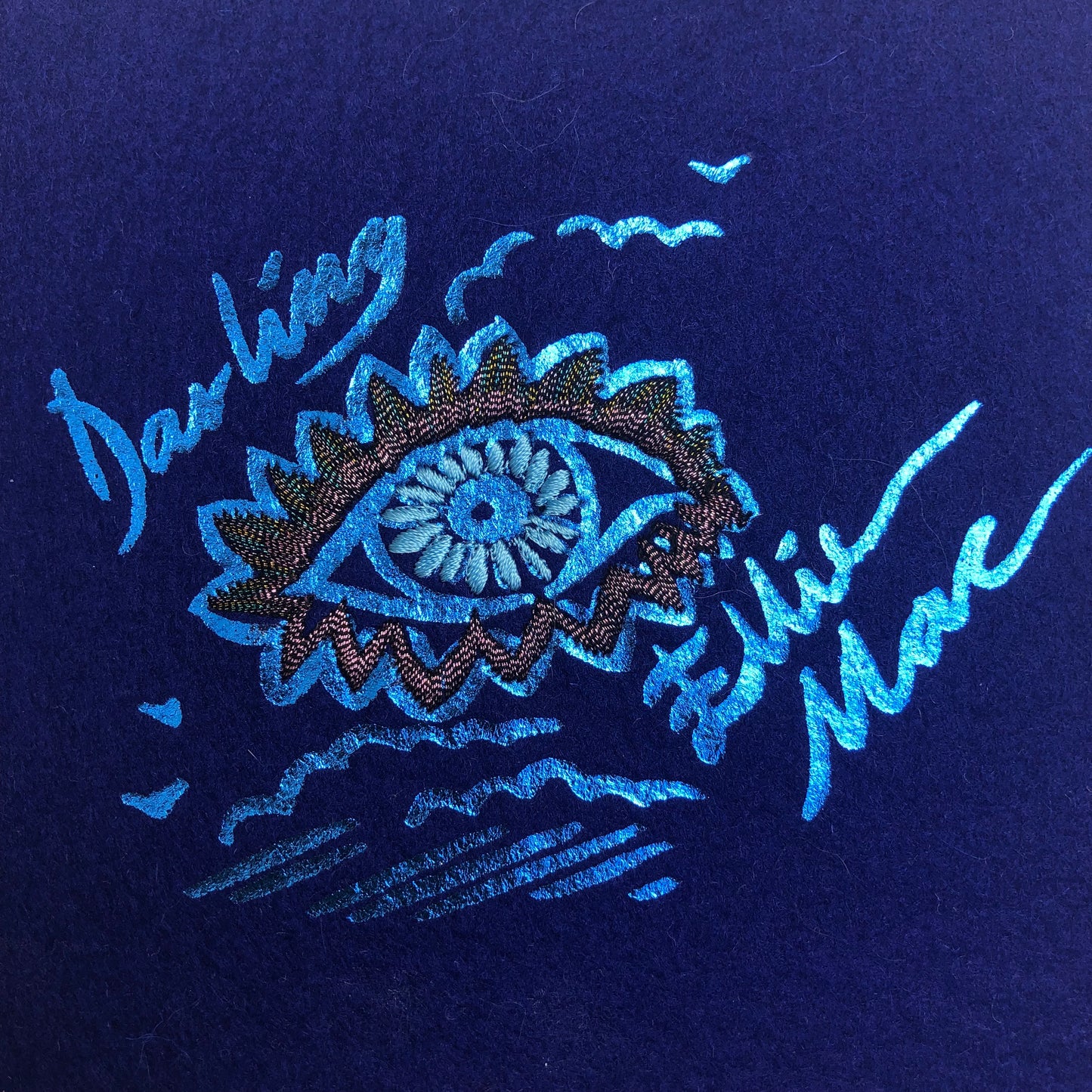 Screen printed signtures for Ellie Mac and Sophie Darling, printed in blue ink on blue felt. The signatures are above and below a printed eye with embroidered eyelash details