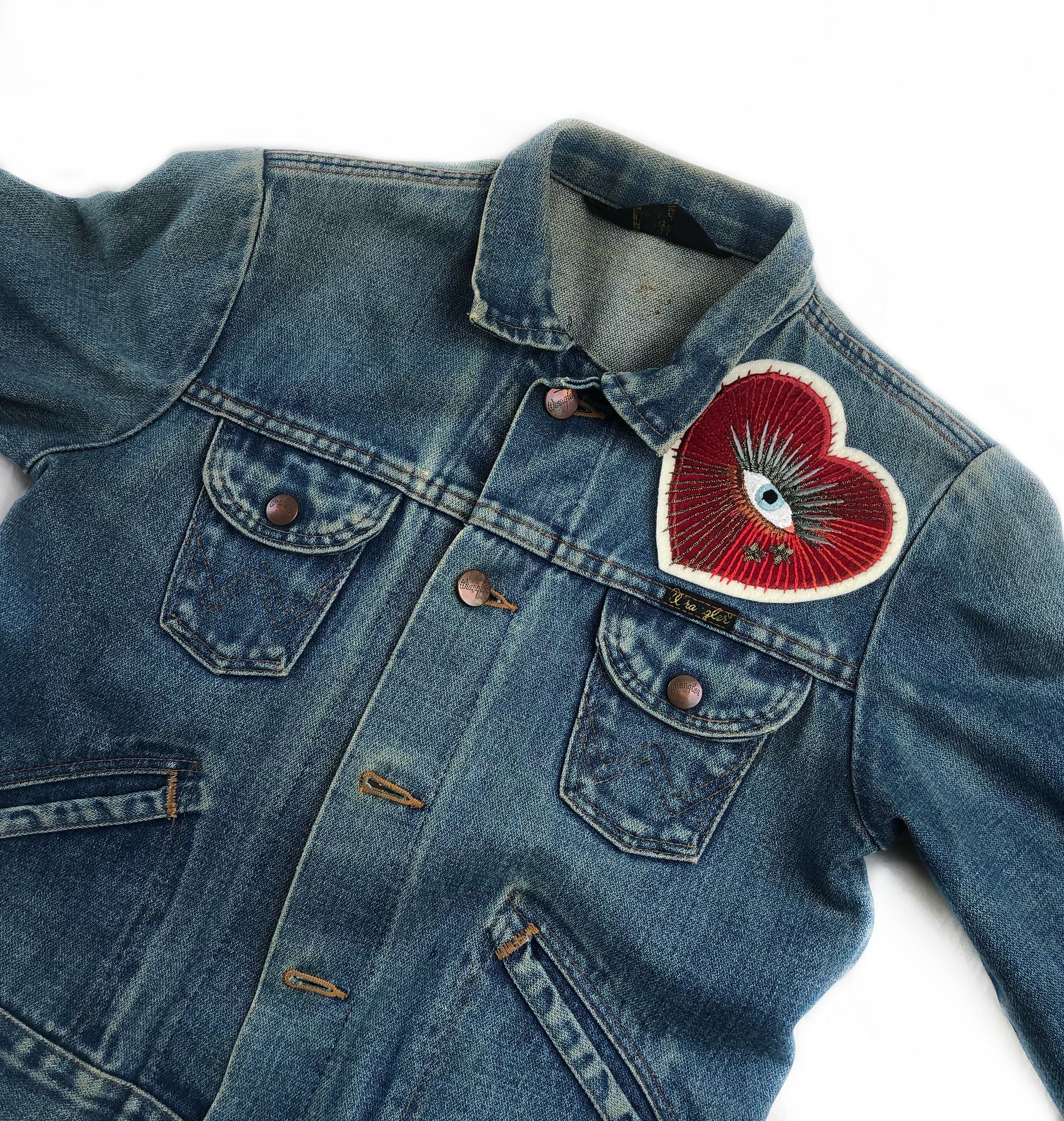 Sacred heart with eye embroidered patch on front shoulder of blue denim jacket