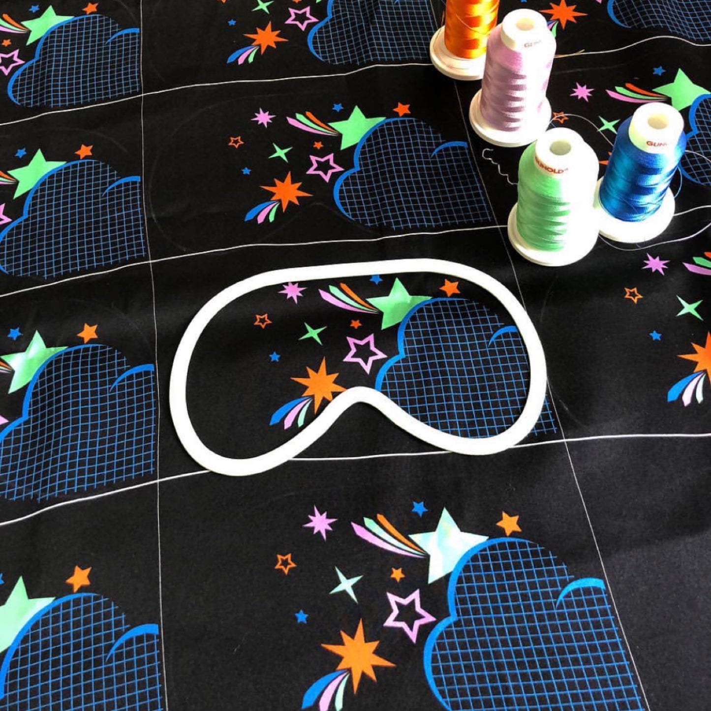 A length of the printed silk satin for the disco nap eye mask, before they are embroidered and cut. Four embroidery threads are placed on the silk fabric