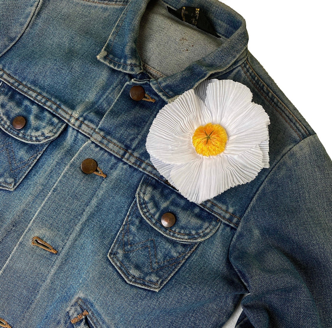 Pleated fried egg flower embroidery on the front shoulder of a blue denim jacket