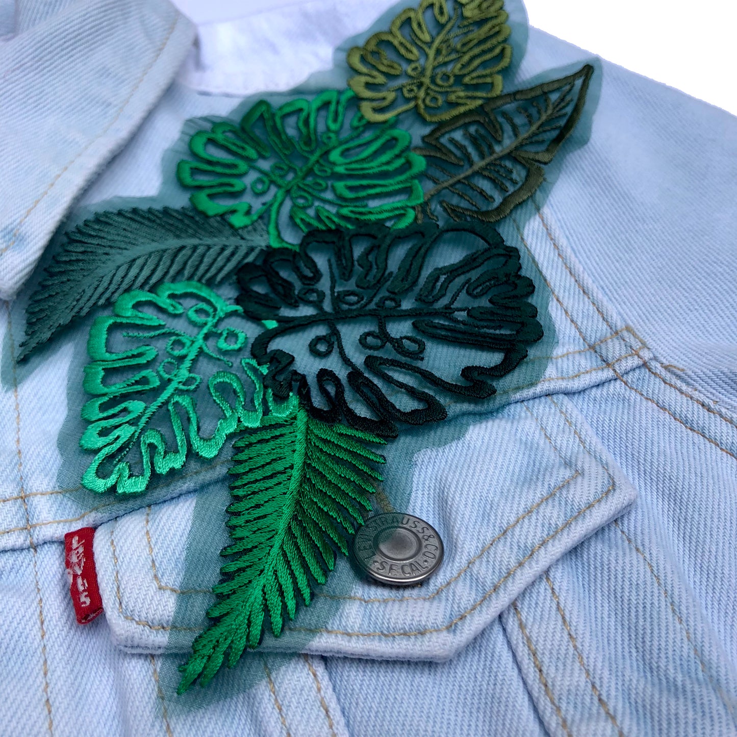 Close-up of sheer silk embroidered leaf piece on shoulder of pale blue denim jacket