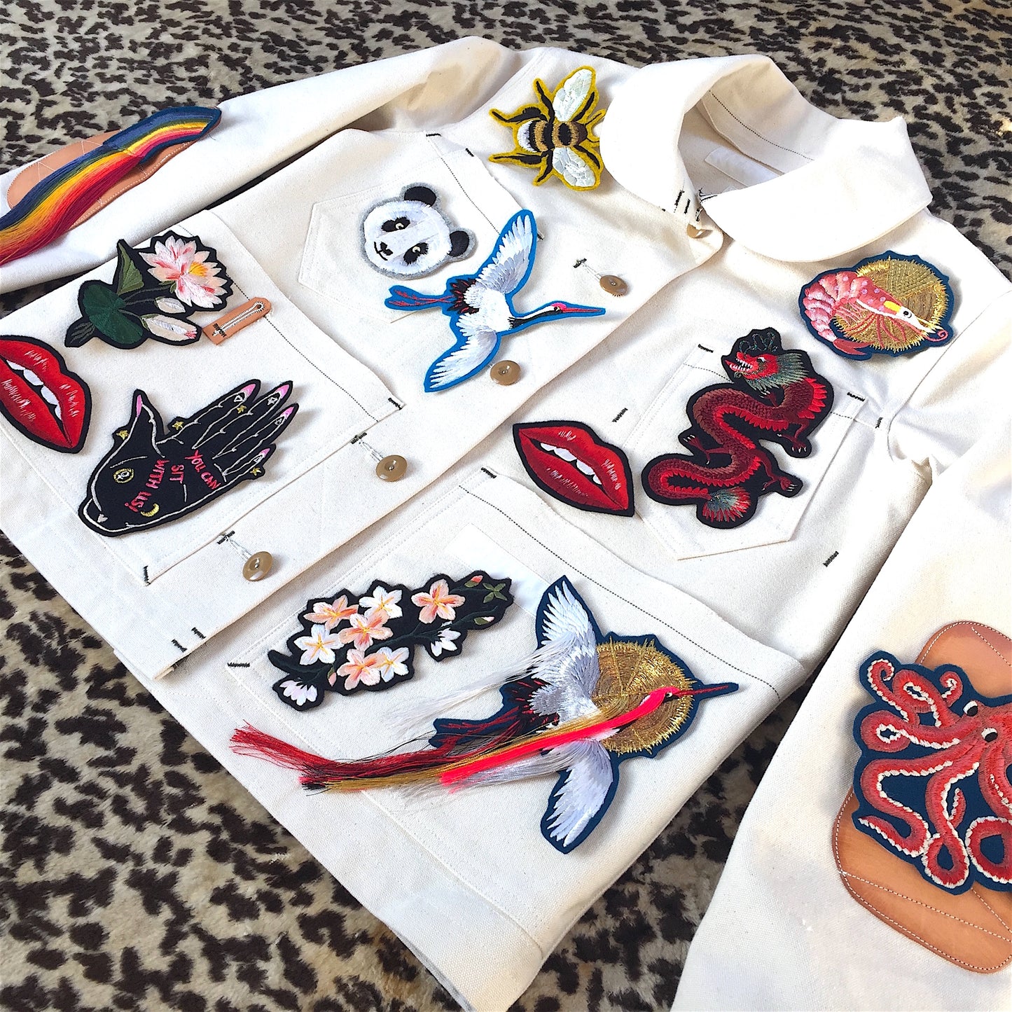 White denim jacket with a number of Ellie Mac embroidered patches including fringed crane, gold bee, panda face and an octopus on the sleeve