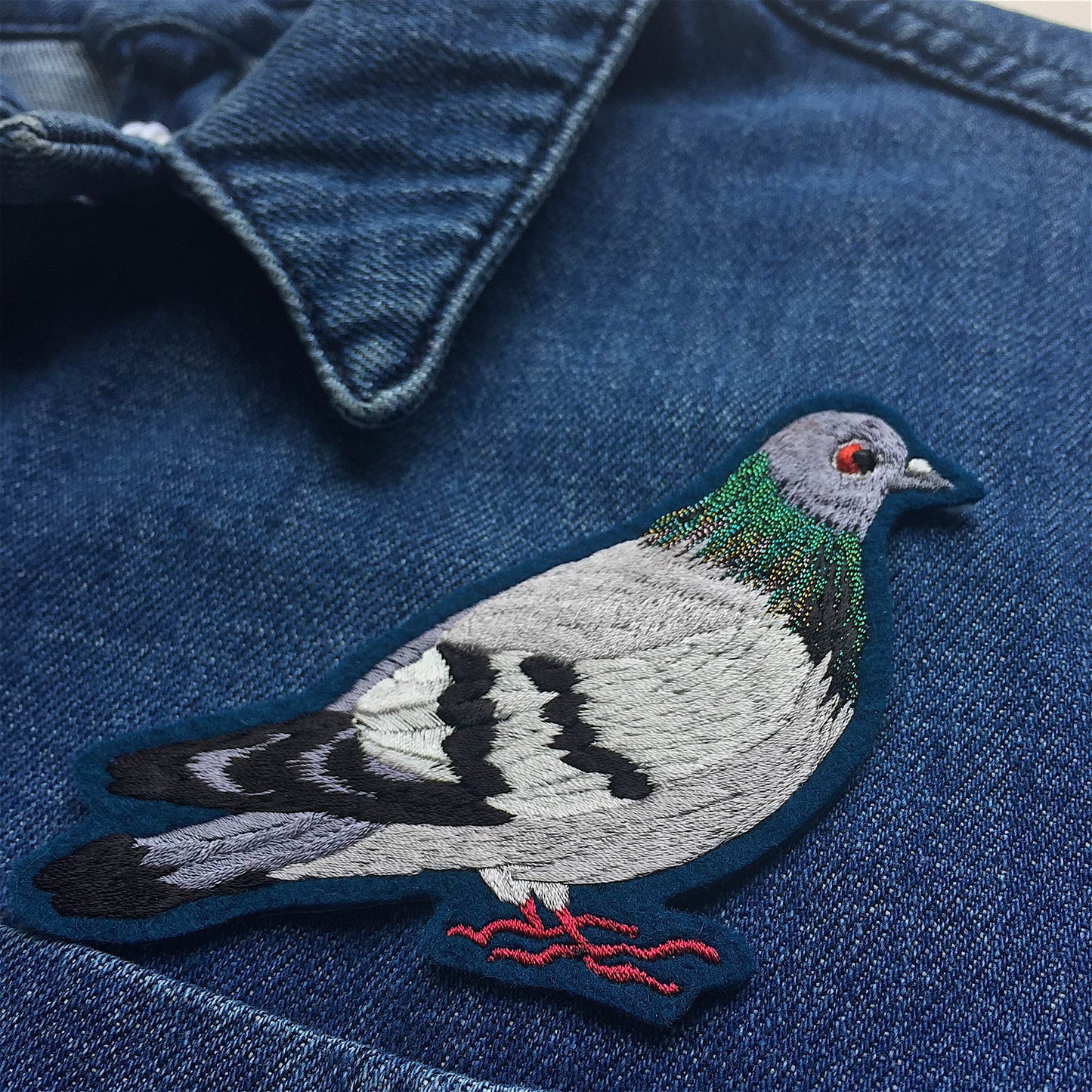 Close-up of the front breast of a dark blue denim jacket with a pigeon embroidered patch on