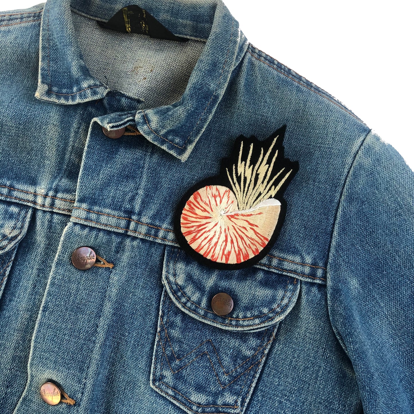 Metallic nautilus shell patch on front shoulder of blue denim jacket