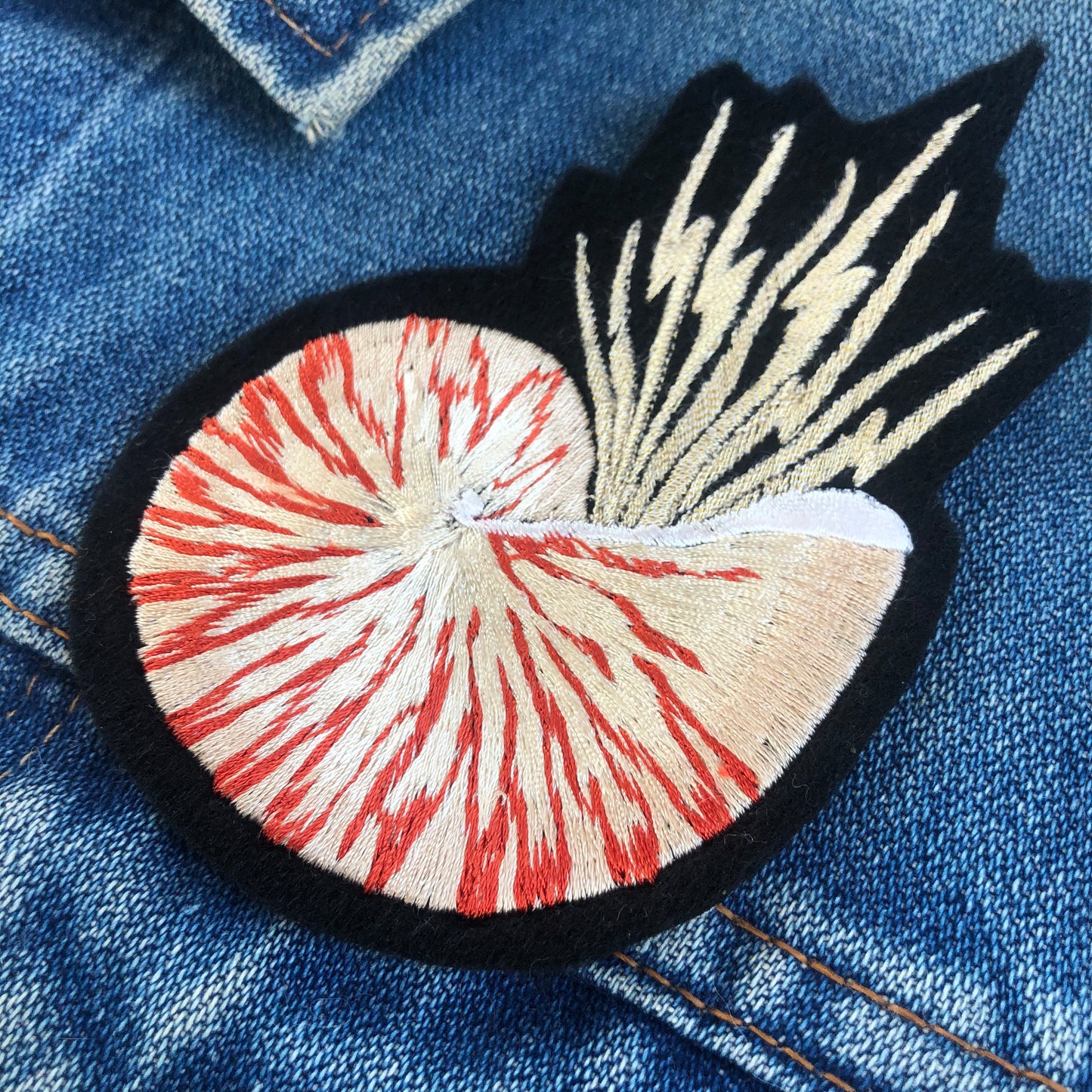 Close-up of metallic nautilus shell patch on blue denim jacket